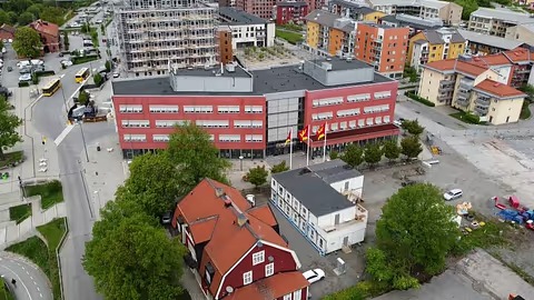 Vy över en modern stadsdel med bostäder och byggnader omgiven av träd.