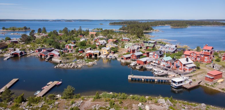 Vy över en pittoresk kustby med färgglada hus vid vattnet och omgivande natur.