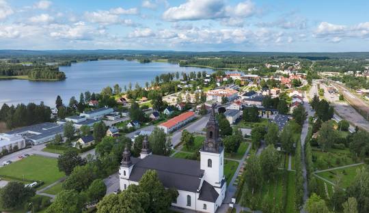 Vy över en stad nära en sjö med grönskande träd och en kyrka i förgrunden.