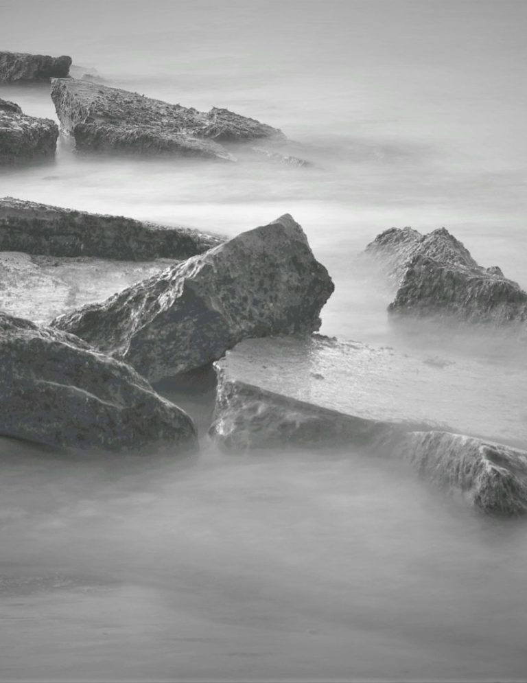 Grå stenar vid vattenkanten med mjuka vågor som sköljer över dem.