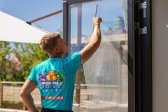 En person i blå tröja rengör ett fönster med en grund.