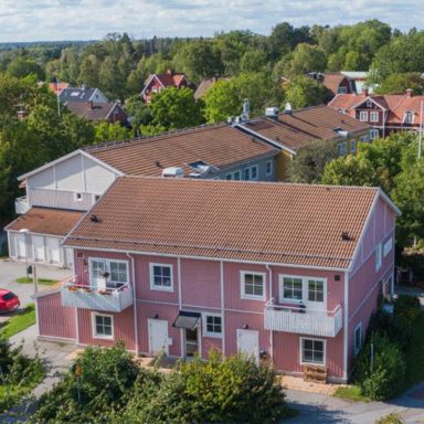 Rödaktig byggnad med vita detaljer omgiven av grön natur och villor.