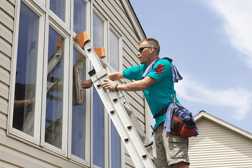 Svåråtkomliga fönster med stege Man på stege som arbetar med fönster i ett hus.