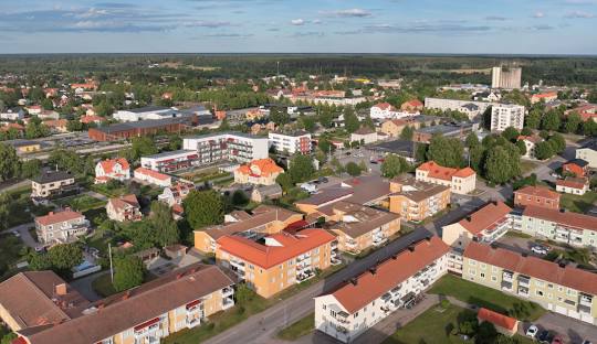 Översiktsvy över en liten stad med tak och grönområden under en blå himmel.