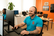 Man with headset working at a computer in a bright office environment.