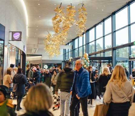 Folkmassa i en modern butik med stora fönster och dekorativa lampor i taket.